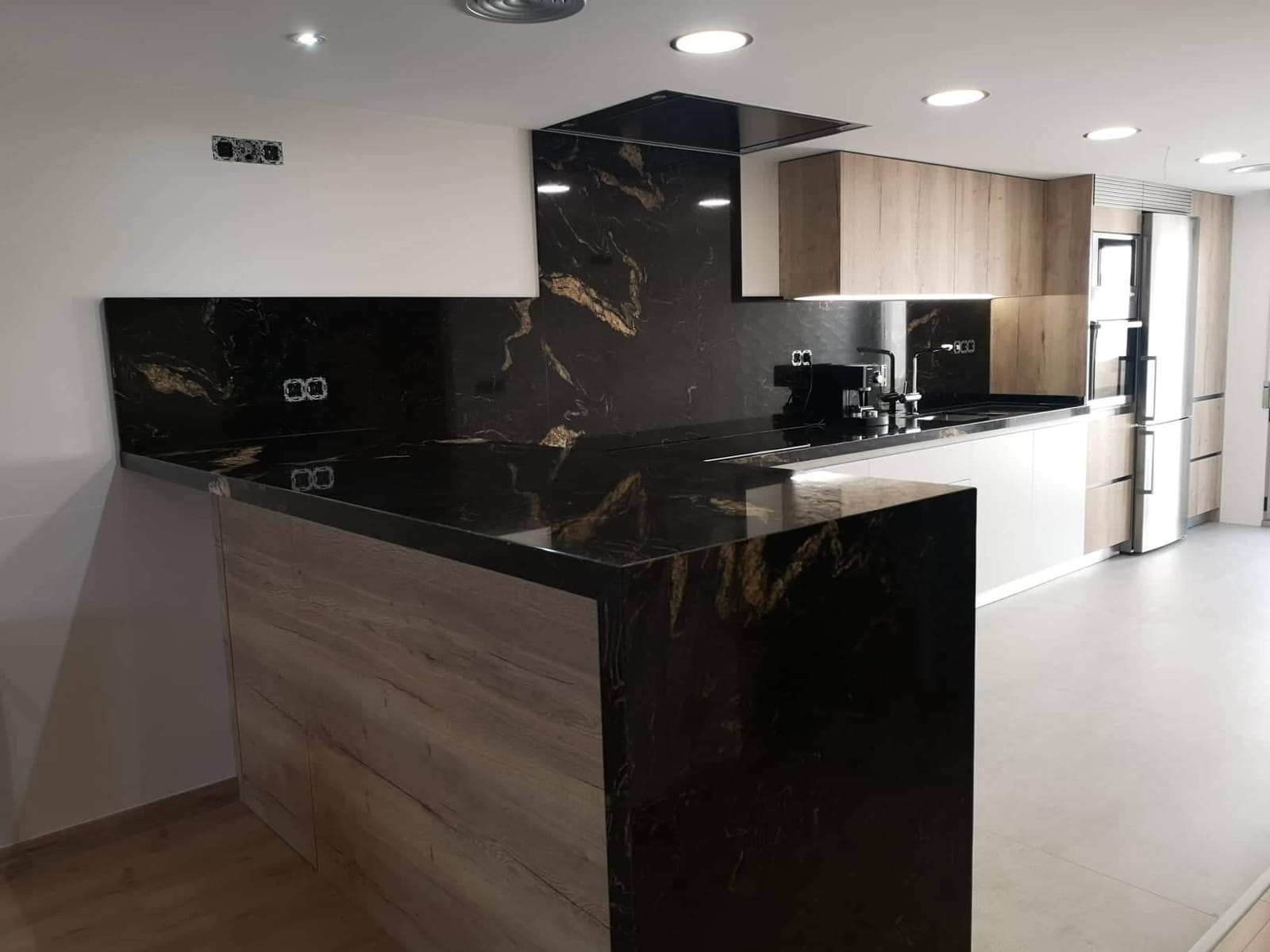 Cocina con península de piedra negra y frentes de madera